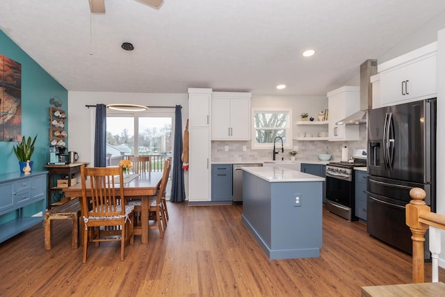 kitchen with open shelves, wall chimney range hood, light countertops, stainless steel appliances, and a kitchen island