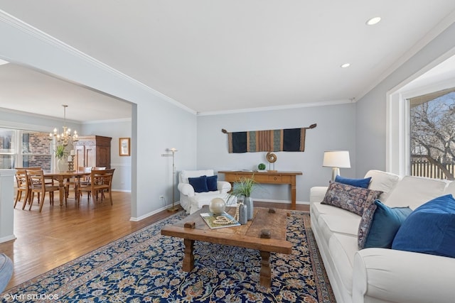 living area featuring a notable chandelier, crown molding, wood finished floors, baseboards, and recessed lighting