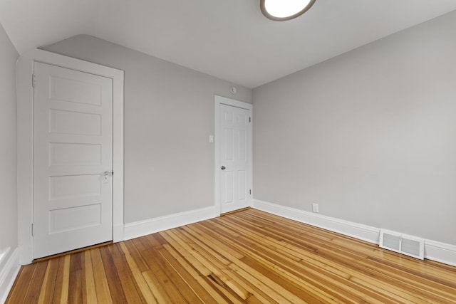 unfurnished room with baseboards, light wood-style flooring, visible vents, and vaulted ceiling