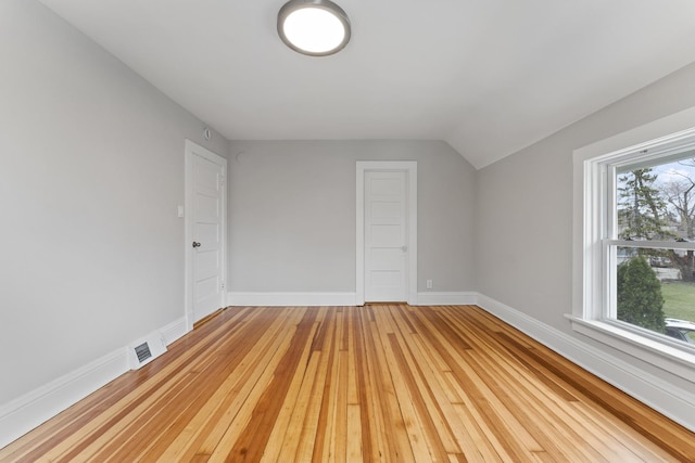 unfurnished room with baseboards, lofted ceiling, visible vents, and light wood-type flooring