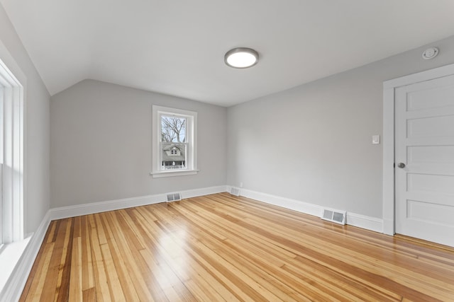 unfurnished room with baseboards, visible vents, light wood-style floors, and lofted ceiling