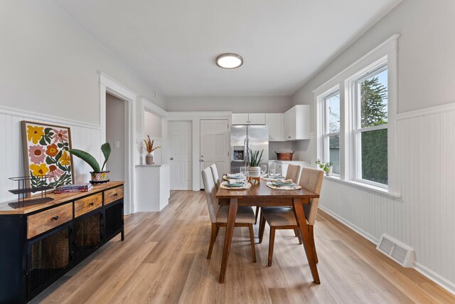 dining space with light wood-style flooring, visible vents, and wainscoting