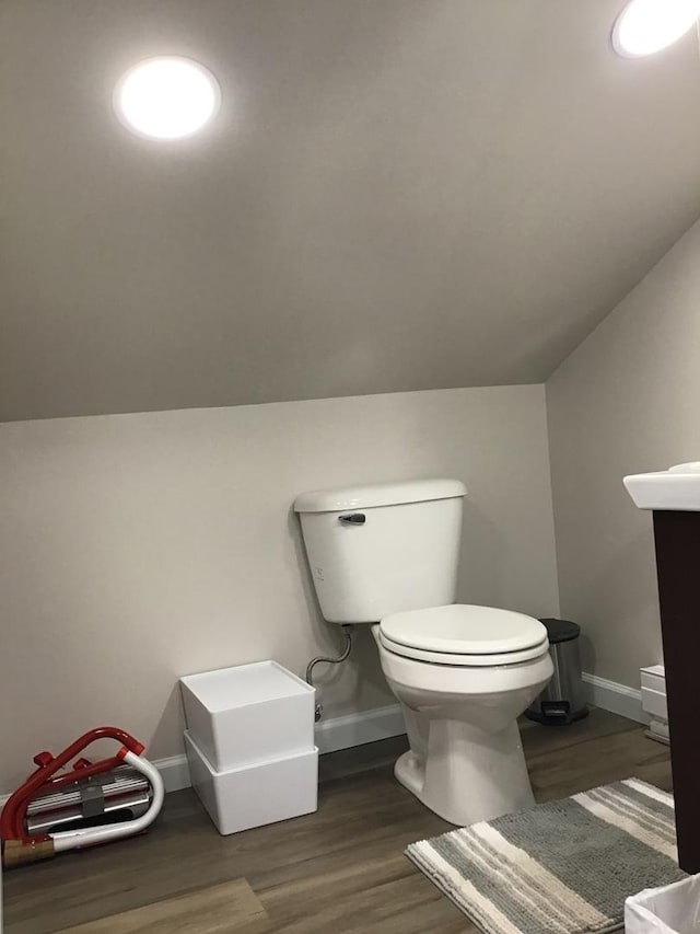 half bath with toilet, baseboards, vaulted ceiling, and wood finished floors