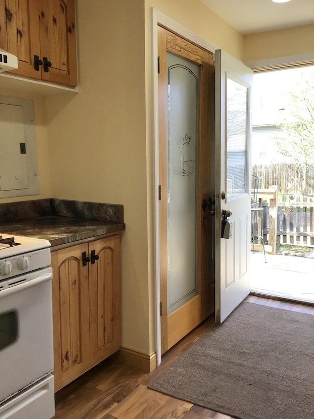 kitchen with dark wood-style flooring, dark countertops, brown cabinets, baseboards, and white gas range oven