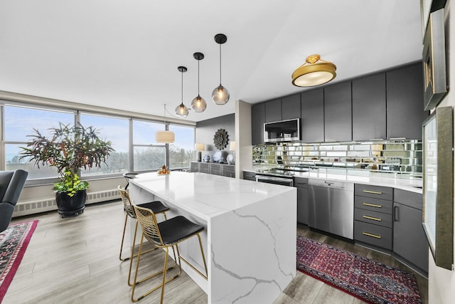 kitchen with light wood-type flooring, a kitchen island, appliances with stainless steel finishes, light stone counters, and backsplash