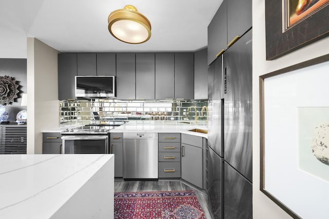 kitchen featuring gray cabinets, decorative backsplash, appliances with stainless steel finishes, and dark wood-style floors