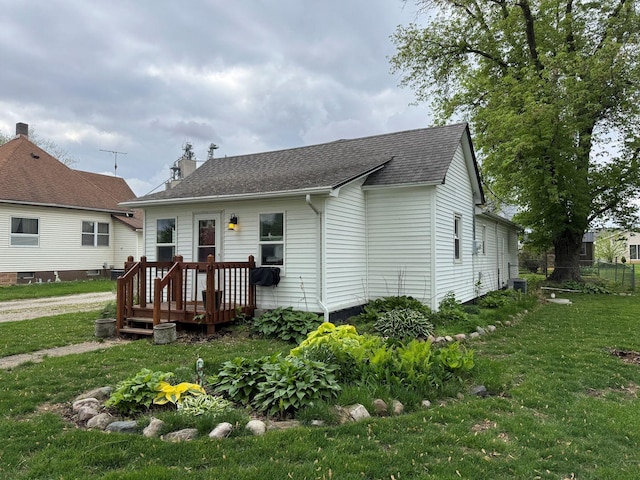 view of front of house with a front yard, a shingled roof, and cooling unit