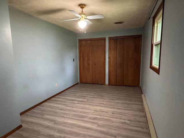 unfurnished bedroom featuring multiple closets, a baseboard heating unit, a textured ceiling, light wood-style flooring, and baseboards