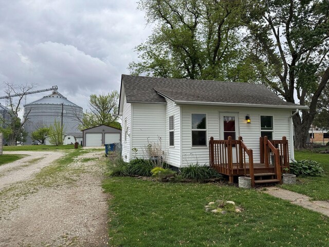 bungalow-style home with an outbuilding, a front yard, a garage, and roof with shingles