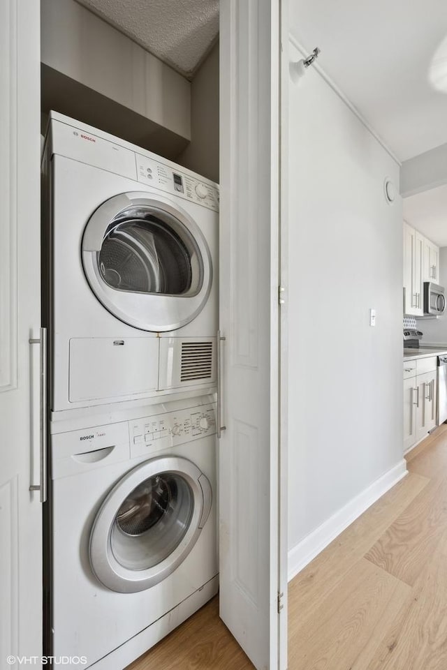 laundry room with laundry area, light wood-style floors, baseboards, and stacked washer / dryer