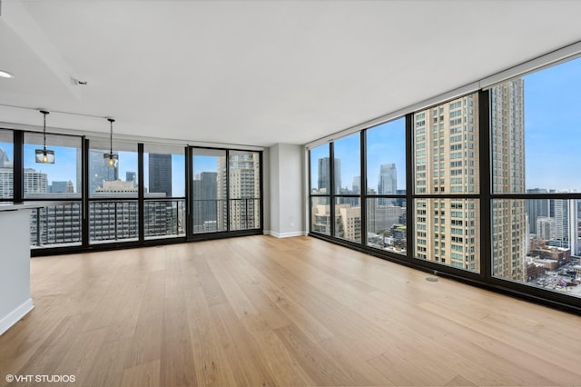 empty room with expansive windows, a view of city, baseboards, and wood finished floors