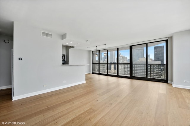 unfurnished living room featuring visible vents, baseboards, expansive windows, and light wood-type flooring