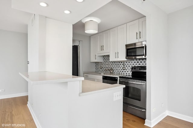 kitchen with a peninsula, light wood-type flooring, light countertops, appliances with stainless steel finishes, and backsplash