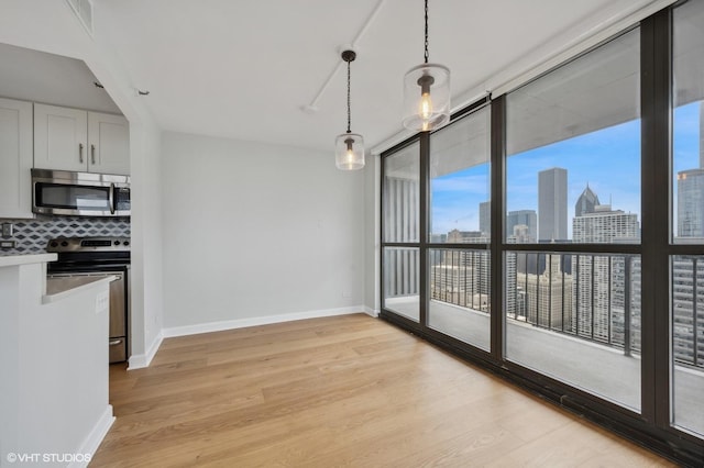 unfurnished dining area with a view of city, baseboards, visible vents, and light wood-type flooring