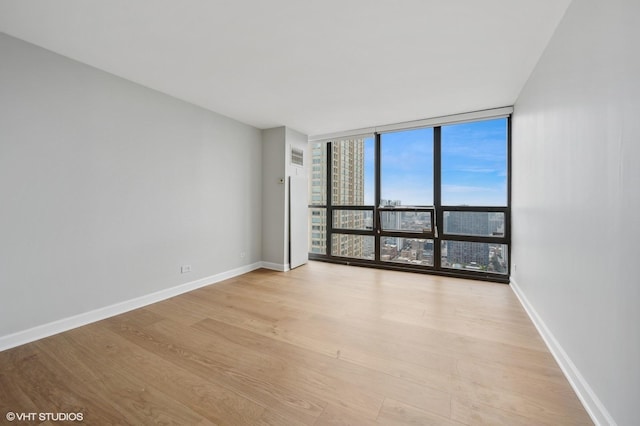 spare room featuring baseboards, visible vents, expansive windows, and light wood-type flooring