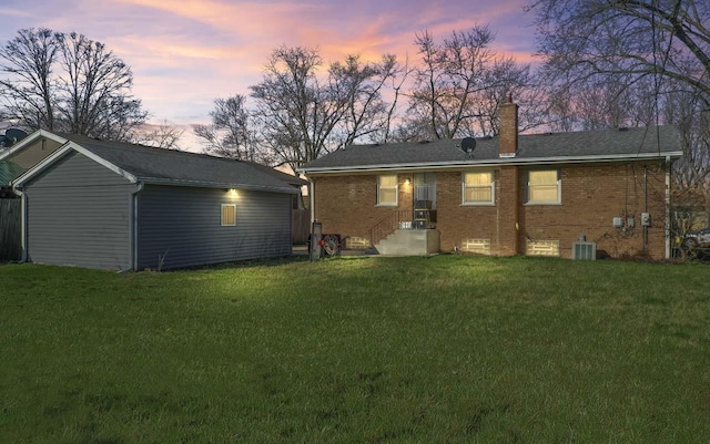 back of property with central AC unit, an outbuilding, a lawn, a chimney, and brick siding