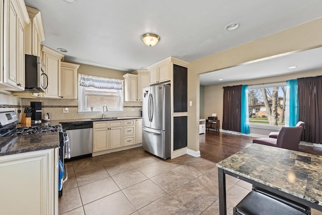 kitchen featuring light tile patterned floors, tasteful backsplash, appliances with stainless steel finishes, a sink, and cream cabinets