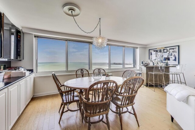 dining space featuring a water view, baseboards, a wealth of natural light, and light wood-type flooring