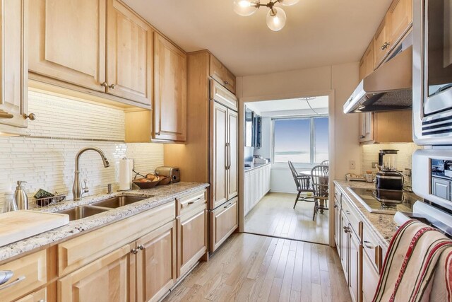 kitchen featuring backsplash, a sink, light wood finished floors, light brown cabinets, and under cabinet range hood