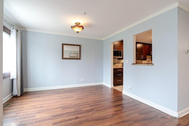 spare room featuring baseboards, visible vents, crown molding, and wood finished floors
