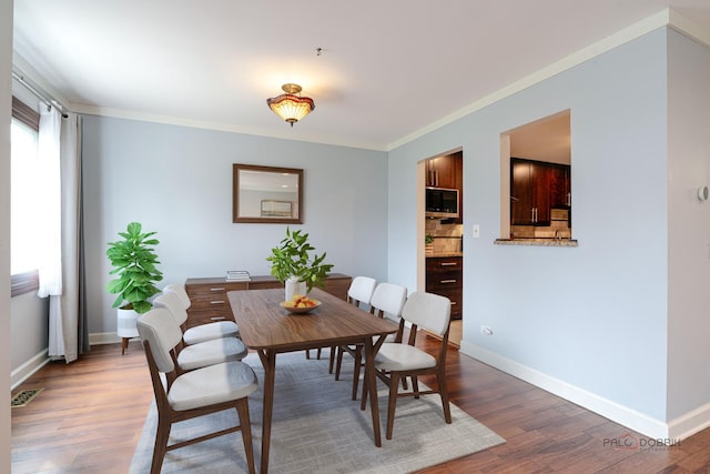 dining room featuring baseboards, ornamental molding, visible vents, and wood finished floors