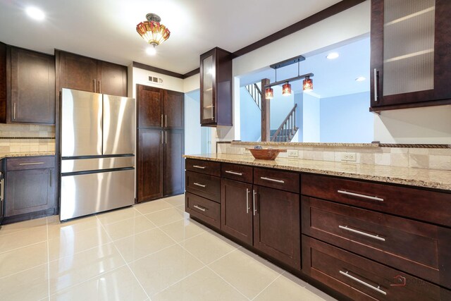 kitchen featuring light stone counters, backsplash, freestanding refrigerator, glass insert cabinets, and light tile patterned floors