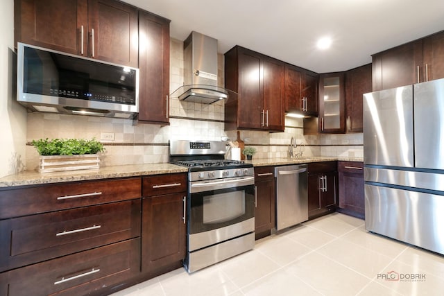 kitchen with light tile patterned flooring, light stone countertops, wall chimney exhaust hood, appliances with stainless steel finishes, and backsplash