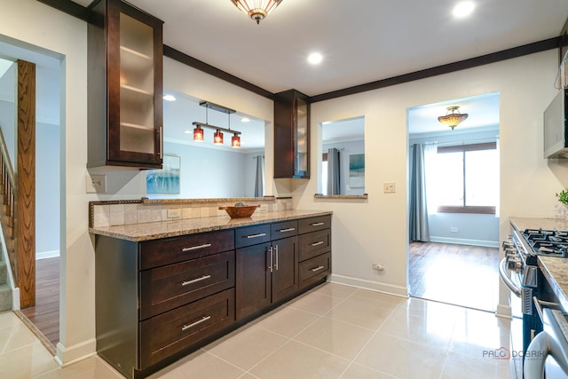 kitchen featuring dark brown cabinets, glass insert cabinets, stainless steel range with gas cooktop, and light tile patterned floors