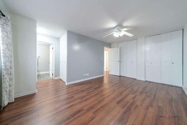 unfurnished bedroom with baseboards, two closets, and dark wood-type flooring