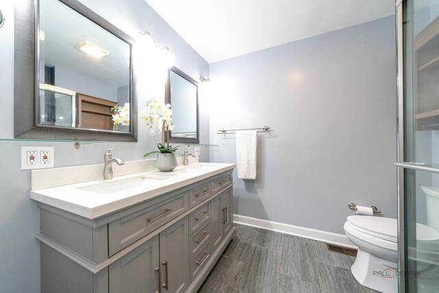 bathroom with baseboards, toilet, double vanity, and a sink
