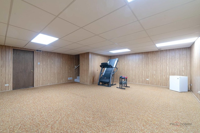 exercise area with wooden walls, carpet floors, and a drop ceiling