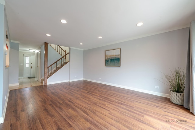 spare room featuring baseboards, crown molding, wood finished floors, and stairway