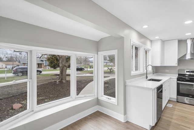kitchen featuring wall chimney exhaust hood, white cabinetry, appliances with stainless steel finishes, light countertops, and a sink