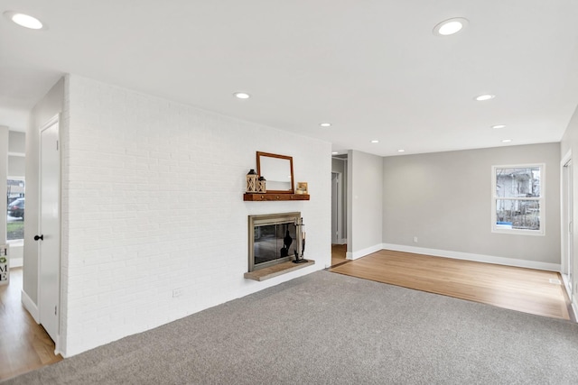 unfurnished living room featuring a glass covered fireplace, brick wall, recessed lighting, carpet, and wood finished floors