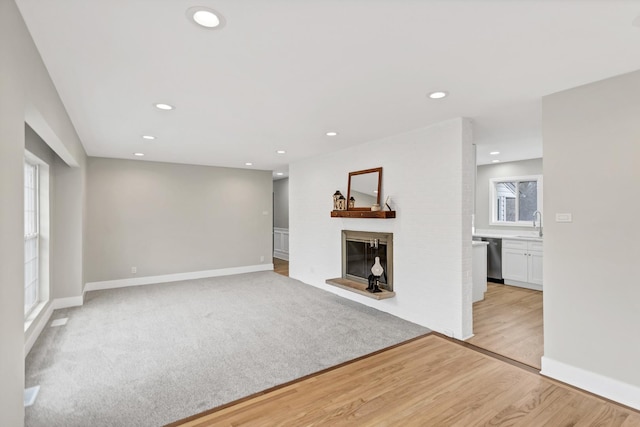 unfurnished living room with light wood-style flooring, recessed lighting, a glass covered fireplace, and baseboards