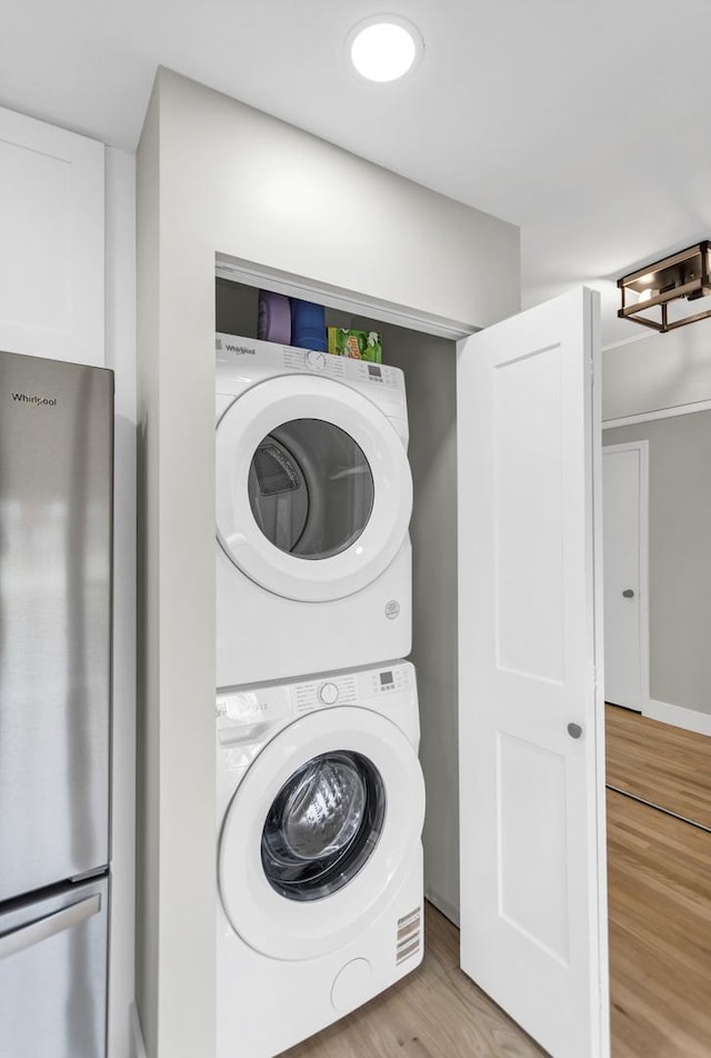laundry room featuring wood finished floors, stacked washer / dryer, and laundry area