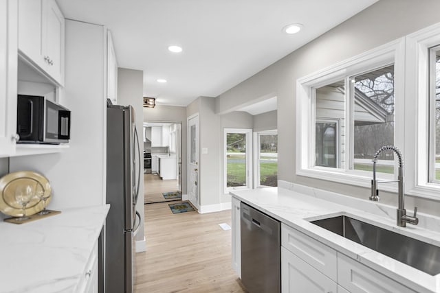 kitchen featuring light stone counters, white cabinetry, stainless steel appliances, light wood finished floors, and a sink