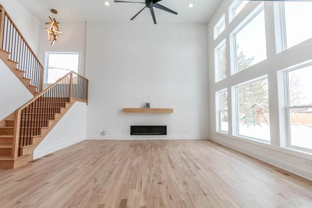 26207 Baxter Dr, Plainfield, IL 60585 - unfurnished living room with light wood-style flooring, stairway, baseboards, ceiling fan, and a high ceiling