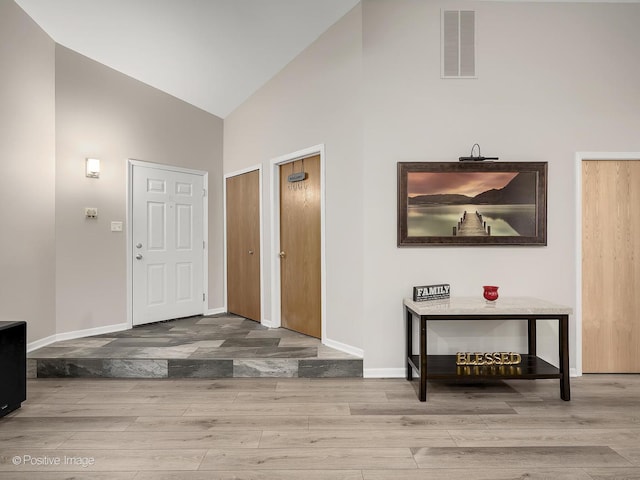 foyer entrance with baseboards, visible vents, high vaulted ceiling, and wood finished floors