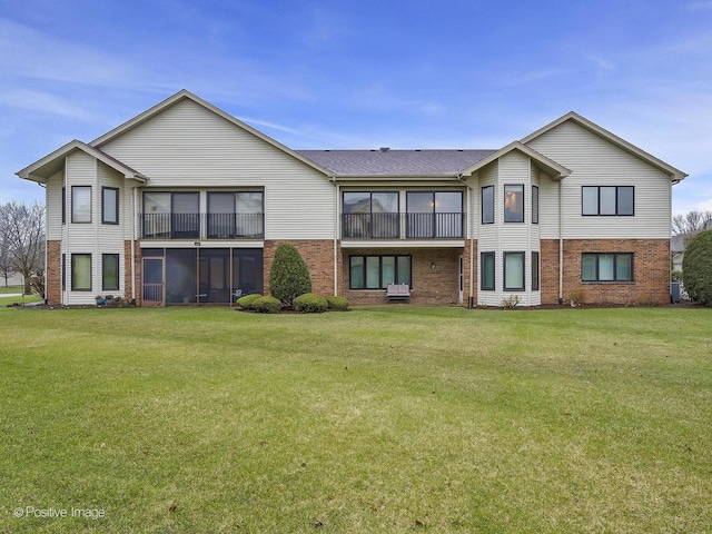 rear view of house with a sunroom, brick siding, and a yard