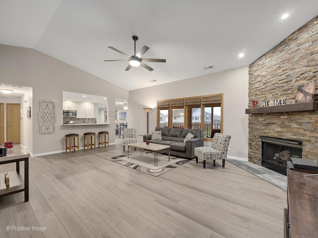 living room with high vaulted ceiling, visible vents, a ceiling fan, a stone fireplace, and light wood-type flooring