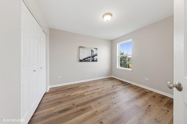unfurnished bedroom featuring wood finished floors, baseboards, and a closet