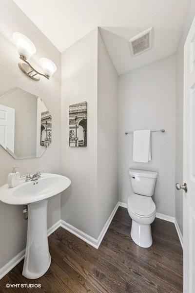half bath with toilet, visible vents, wood finished floors, and baseboards