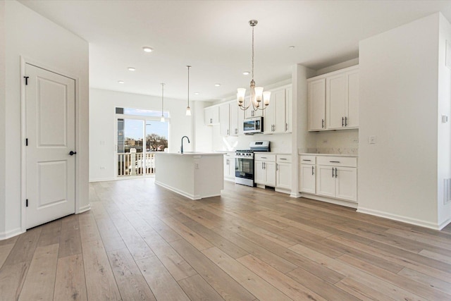 kitchen featuring a chandelier, stainless steel appliances, a center island with sink, white cabinetry, and light wood-type flooring