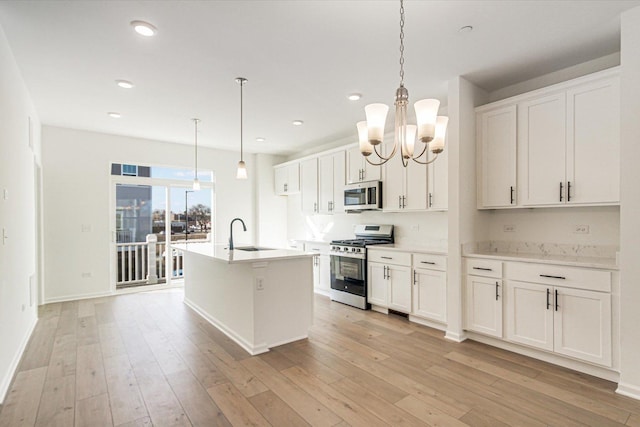 kitchen featuring a sink, a center island with sink, stainless steel appliances, light wood-style floors, and an inviting chandelier