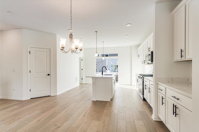 kitchen with light wood finished floors, a kitchen island with sink, stainless steel appliances, a sink, and an inviting chandelier