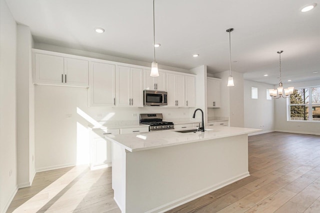 kitchen with light wood finished floors, a center island with sink, appliances with stainless steel finishes, white cabinetry, and a sink
