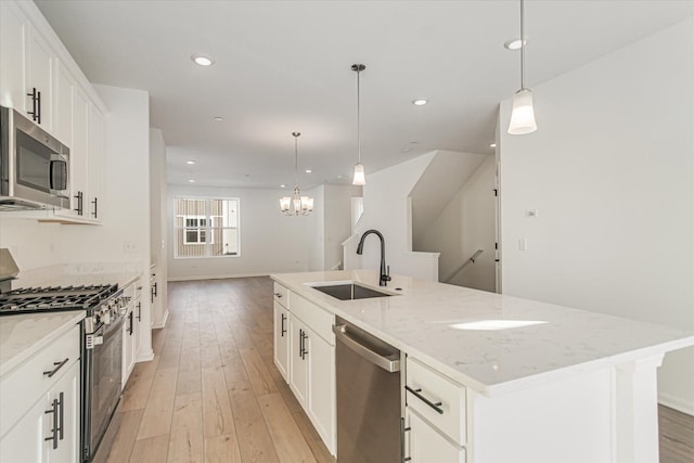 kitchen with a center island with sink, a sink, light wood-style floors, a notable chandelier, and appliances with stainless steel finishes