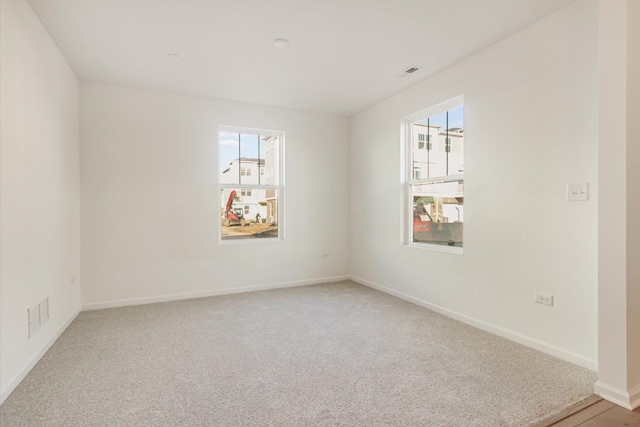 empty room featuring baseboards, visible vents, a healthy amount of sunlight, and light carpet