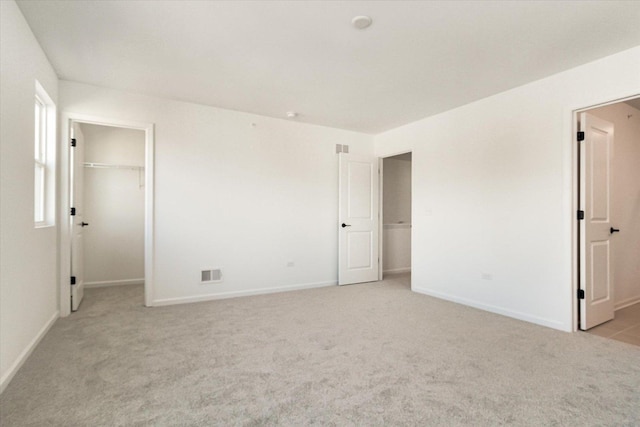 unfurnished bedroom featuring light carpet, baseboards, a walk in closet, and visible vents